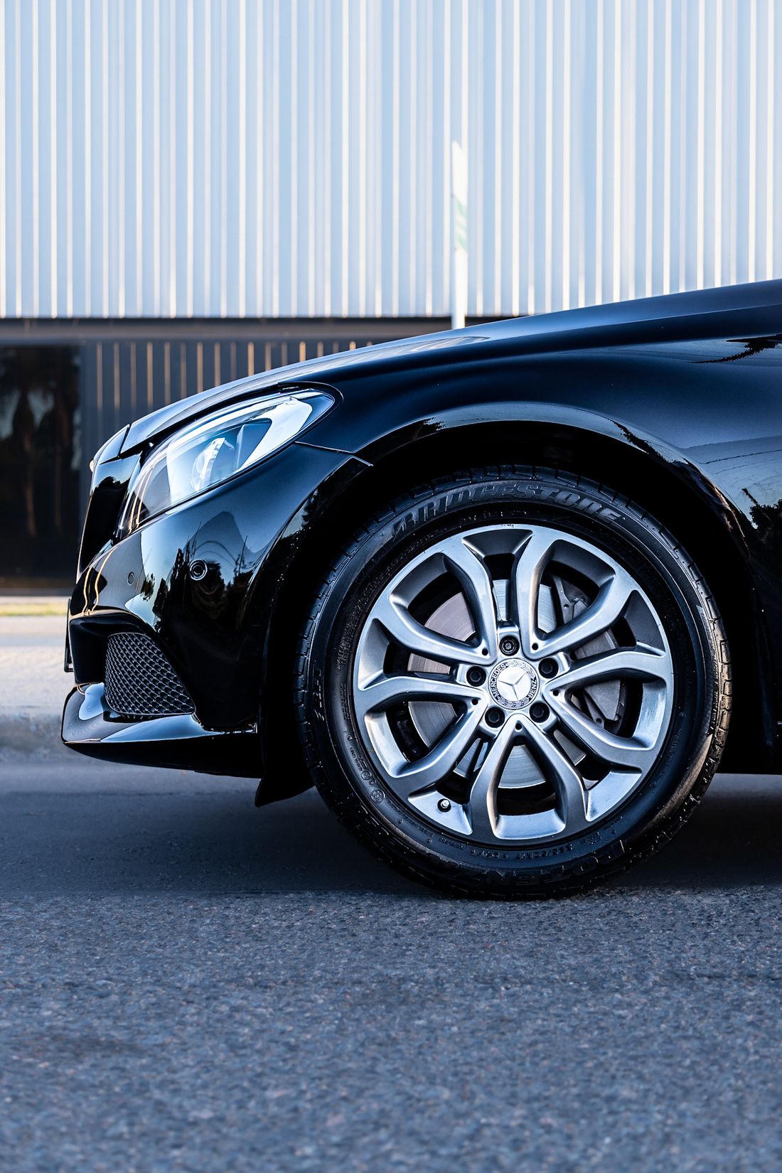 Black car wheel and headlight with reflections across the paint